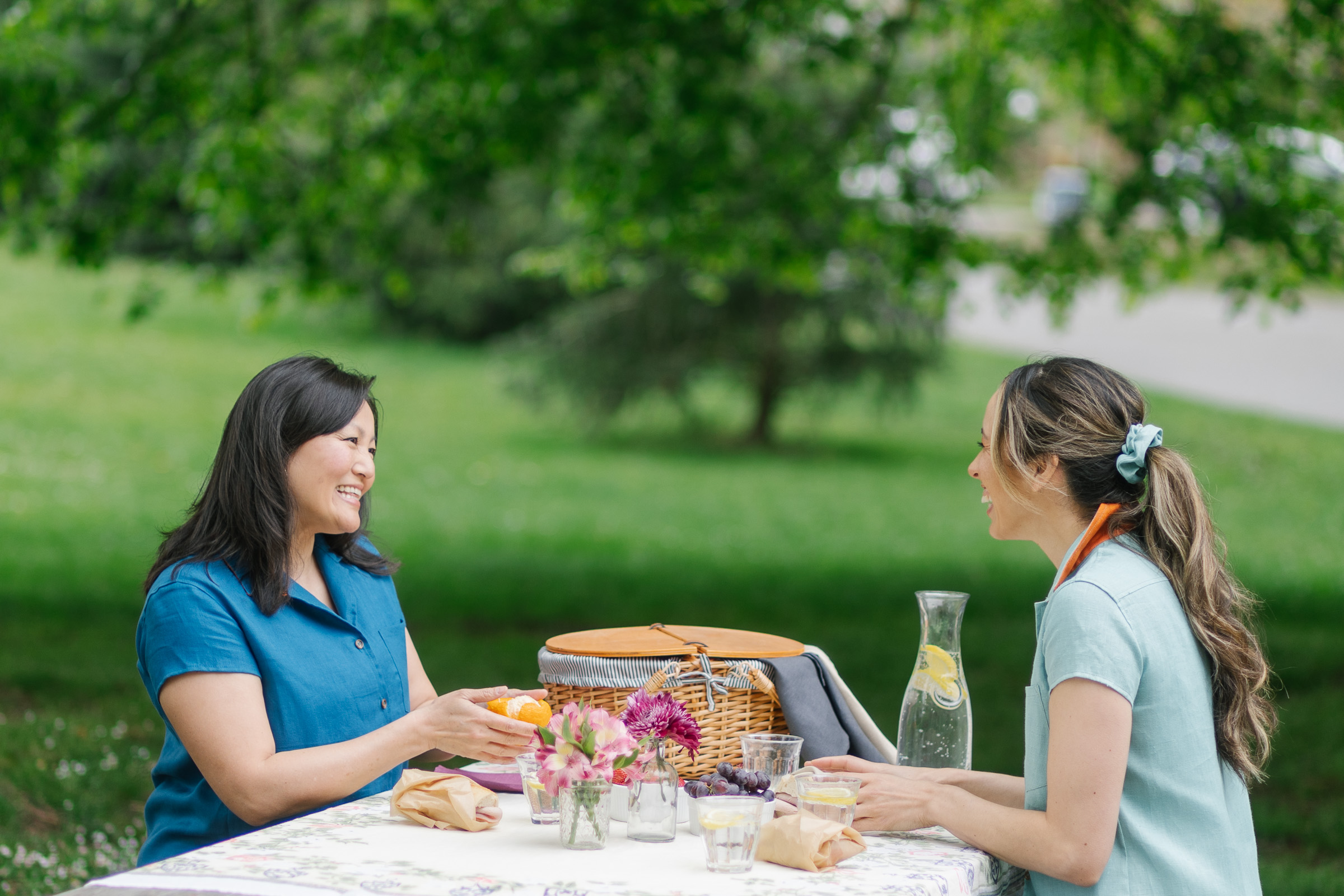 Two friends sit at a beautiful picnic in the summer, laughing and relaxing. Get marketing photography that tells a story for your clothing brand.